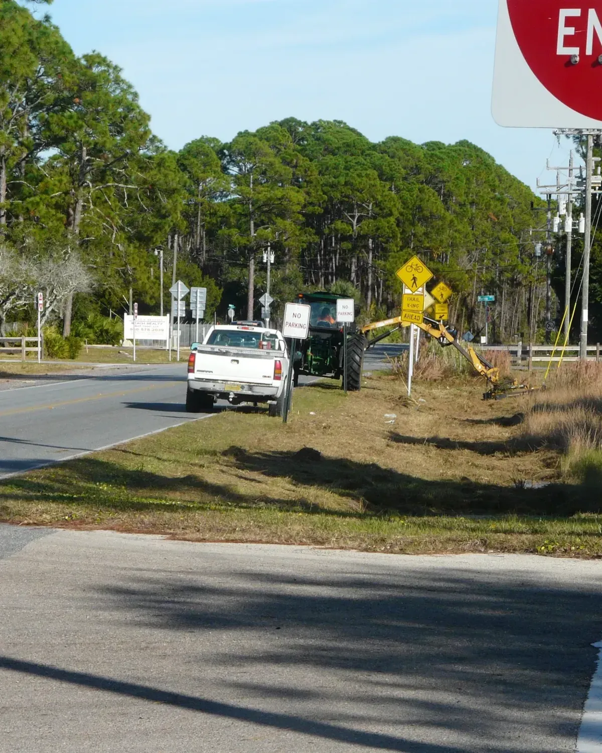 Tractor-mounted boom mower clearing vegetation along a roadside